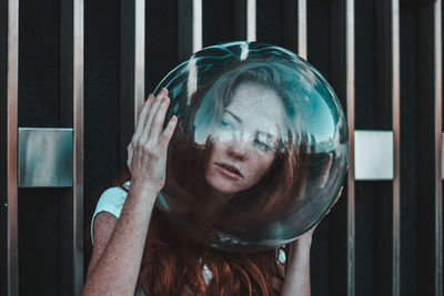 Close-up of thoughtful young woman wearing glass helmet in head against metallic railing