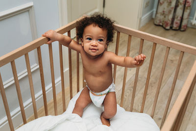 Portrait of shirtless boy in crib at home