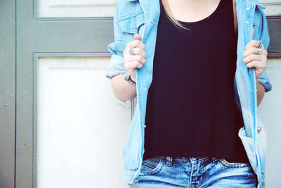 Midsection of woman wearing denim jacket standing against wall