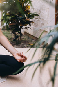 Hand resting on a knee in lotus position, meditating between lush foliage
