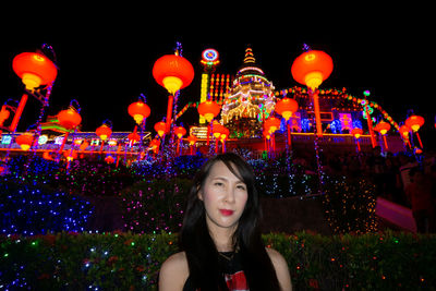 Portrait of woman standing against illuminated lights at night