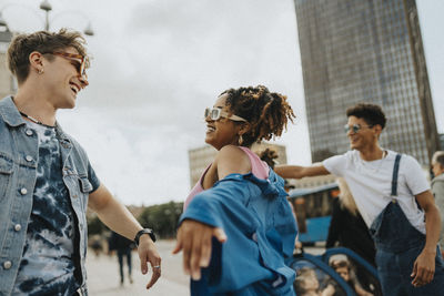 Carefree curly hair woman in sunglasses dancing with male friend on street