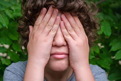 Close-up of boy covering face against leaves