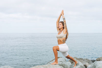 Young woman in white sport clothes practice yoga on sea beach, mental and phisical health