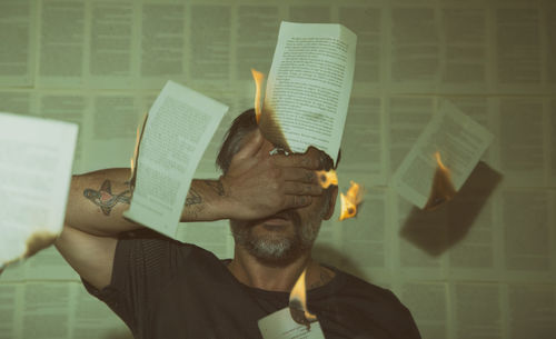 Man covering face while standing amidts burning pages