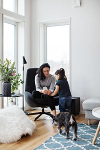 Mother showing mobile phone to daughter while dog walking on floor at home