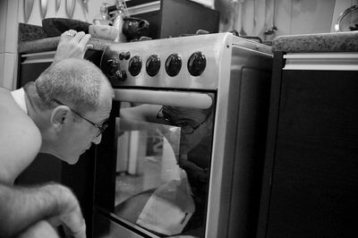 Side view of man looking at oven while crouching in kitchen at home