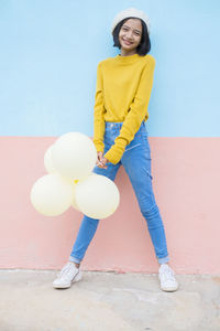 Portrait of a smiling young woman standing against yellow wall