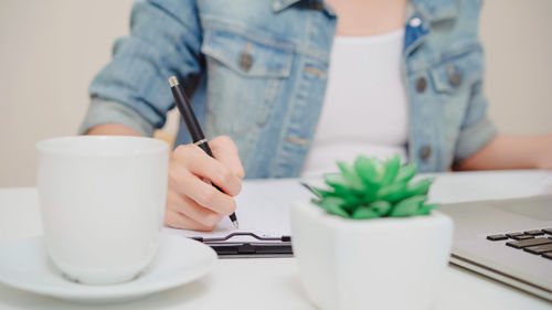 Midsection of woman holding coffee cup on table