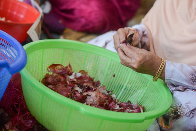 Midsection of woman peeling onion in green basket