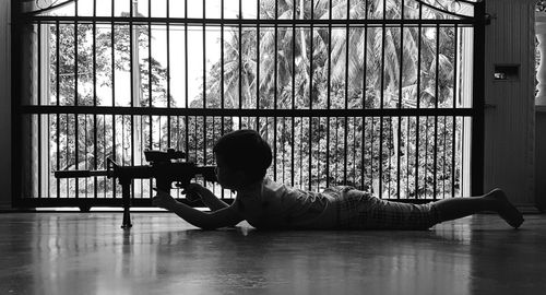 Boy holding rifle while lying on floor at home