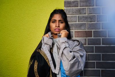 Portrait of young woman standing against wall