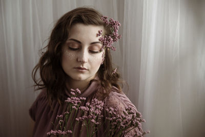 Woman wearing flowers looking down against curtain