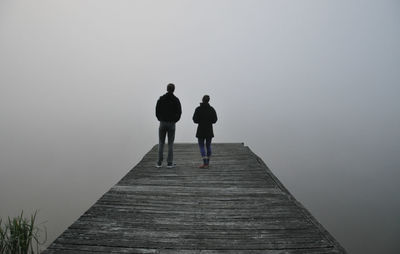 Rear view of couple standing on pier during foggy weather