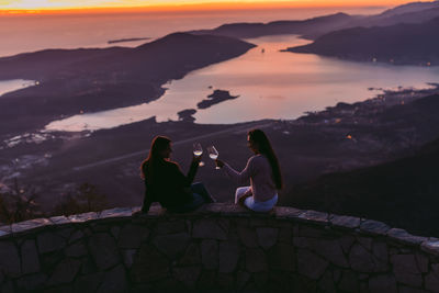 People sitting on mountain against sky during sunset