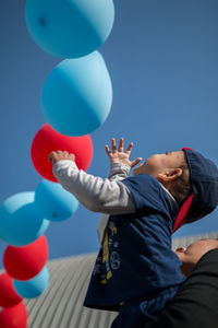 Low angle view of boy balloons against blue sky