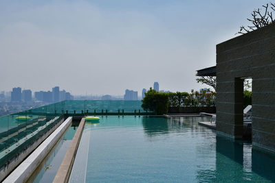 Swimming pool by city against sky