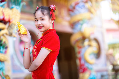 Portrait of smiling girl holding golden bag while sanding outdoors