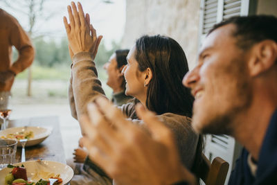 Happy friends clapping during dinner party at patio