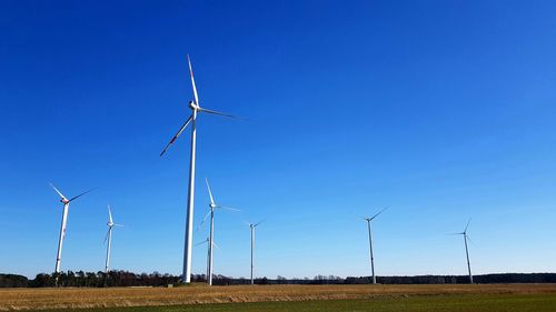 Windmills on field against clear blue sky