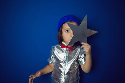 Christmas boy child holding a star in a silver shirt blue hat and red bow tie stands in the studio