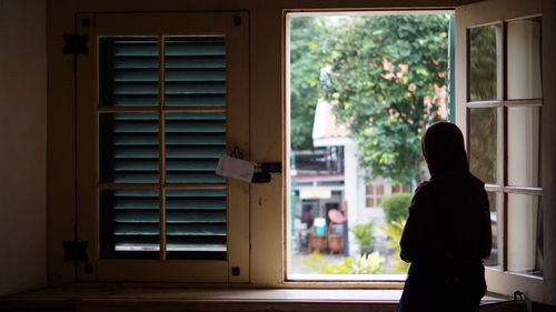 Rear view of woman standing by window in house