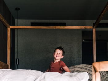 Positive little kid on wooden canopy bed while having fun in bedroom and looking at camera