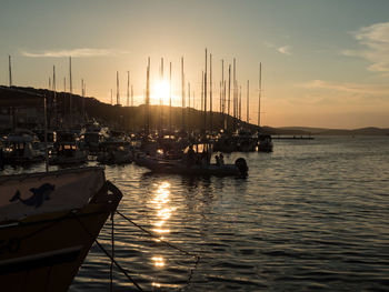 Sailboats moored in harbor at sunset