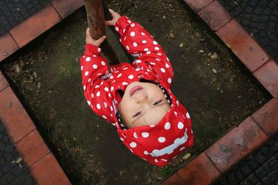 High angle view of girl in red raincoat holding tree trunk during rainy season