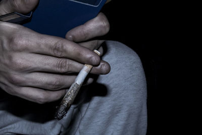 Midsection of person holding burnt cigarette in darkroom