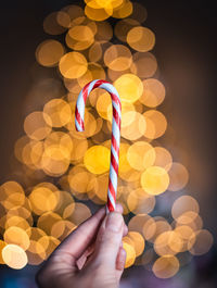 Close up of hand holding candy cane with light bokeh in background.