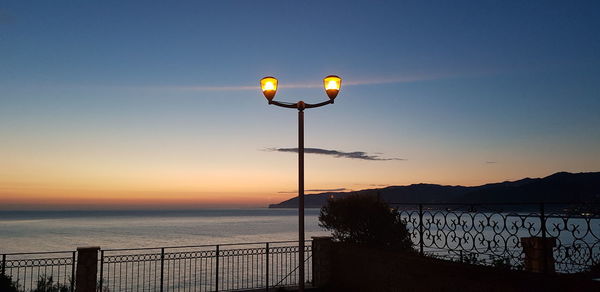 Street light by sea against sky during sunset