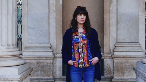 Young woman looking away while standing against wall