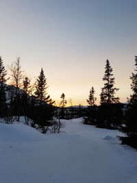 Snow covered field against sky during sunset