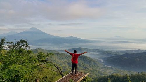 Rear view of man with arms outstretched standing against mountains