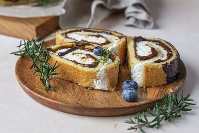 Sponge cake roll with chocolate and cream cheese decorated with glaze, blueberry and rosemary.