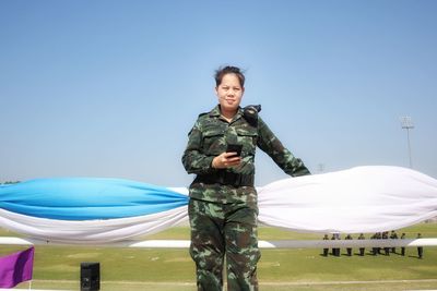 Portrait of female soldier standing against blue sky