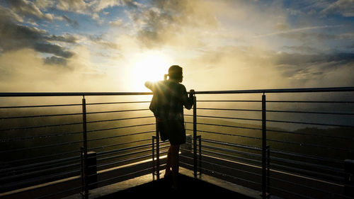 Silhouette man standing by railing against sea during sunset