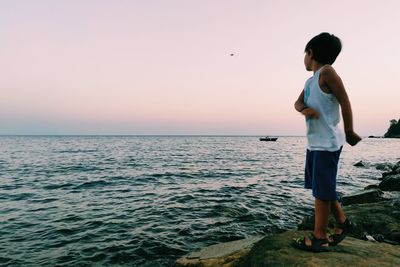 Boy throwing stone in sea against sky