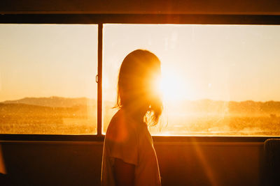 Woman looking through window at sunset