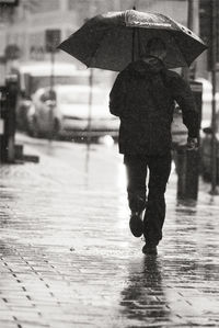 Rear view of man holding umbrella running on street during rainy season