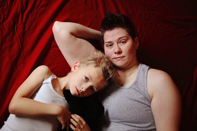 Portrait of mother and son with puppy lying on red fabric