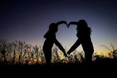 Silhouette couple holding heart shape against sunset sky