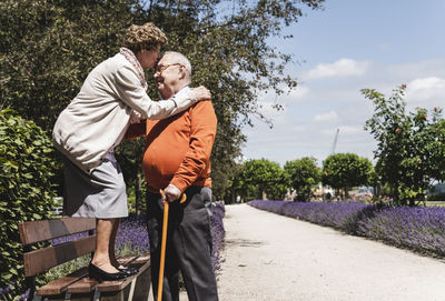Senior couple having fun in the park, woman standing on bench kissing senior man on forehead