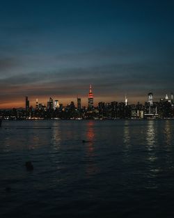 Illuminated buildings by sea against sky at night