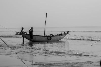 People standing by boat in sea against clear sky