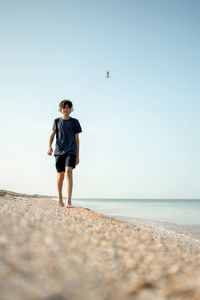 Rear view of woman walking on beach against clear sky