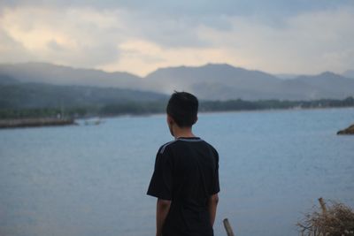 Rear view of man looking at lake against sky