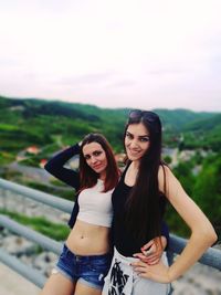 Portrait of smiling friends leaning on railing against clear sky