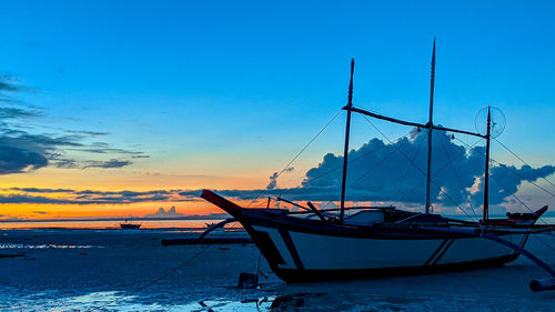 Sailboats moored on sea against sky at sunset